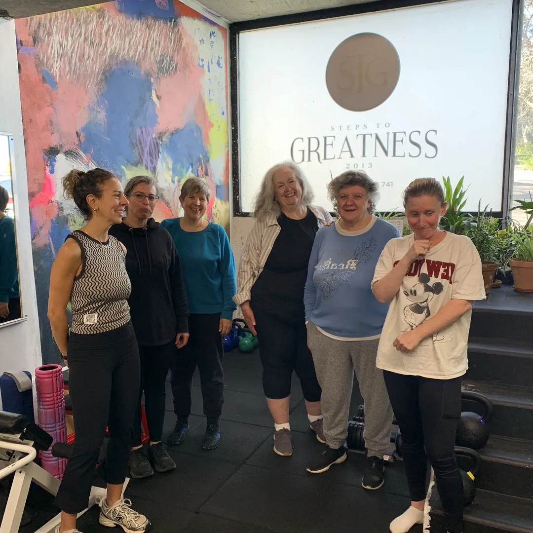 Six women standing together in the studio under the Steps to Greatness sign.