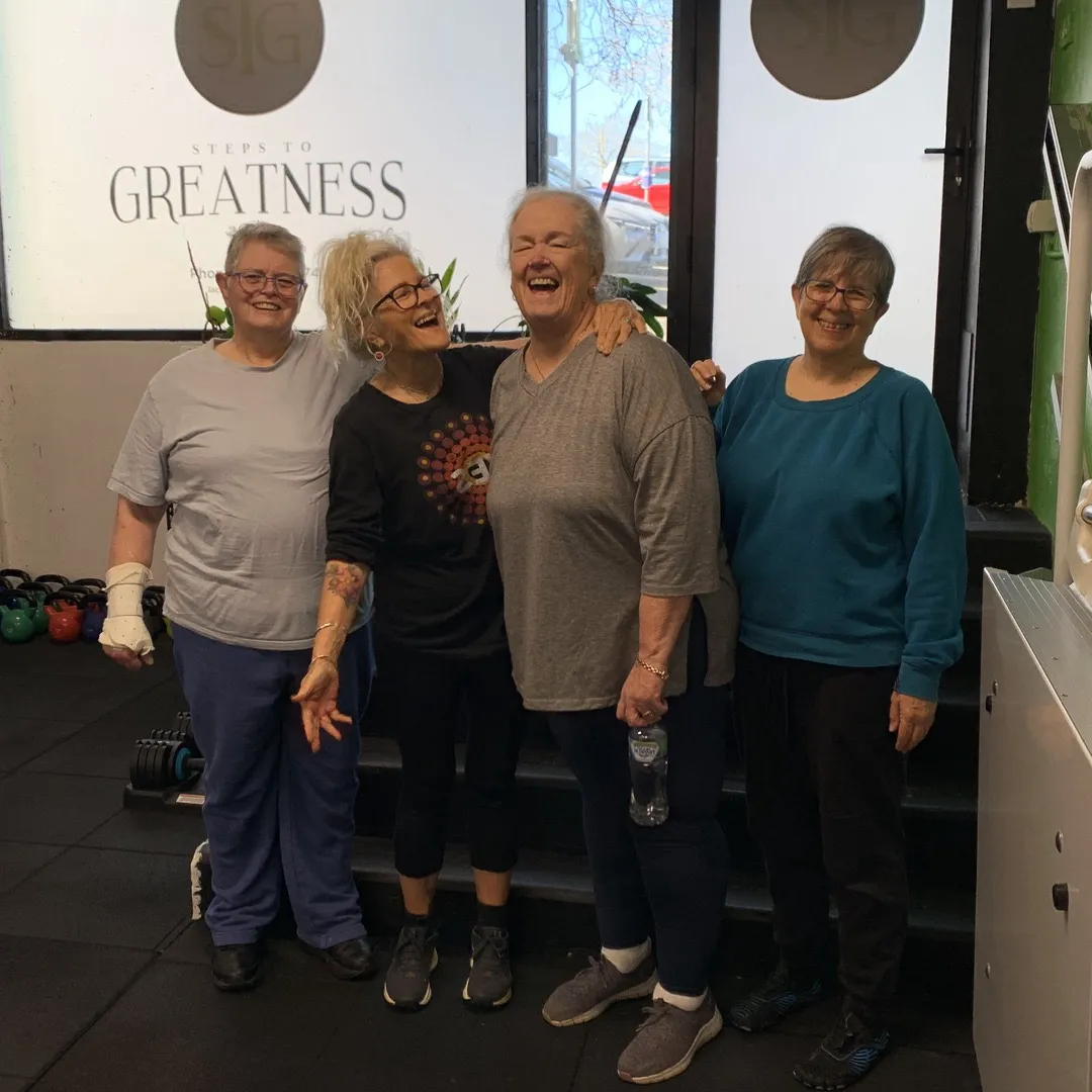 Four women standing arm in arm at the studio door, laughing.