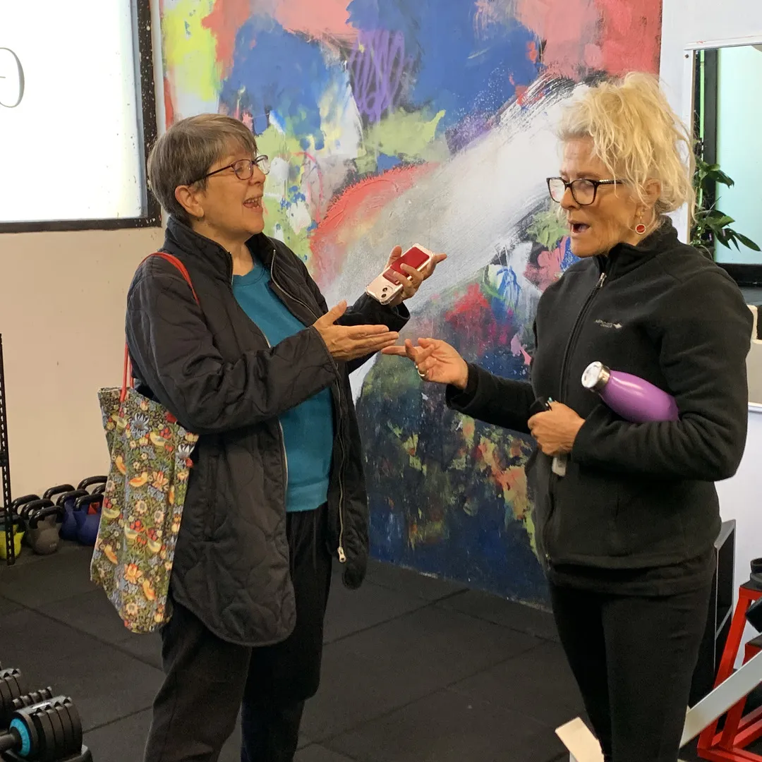 Two women mid-conversation in the studio, in front of the painted wall.