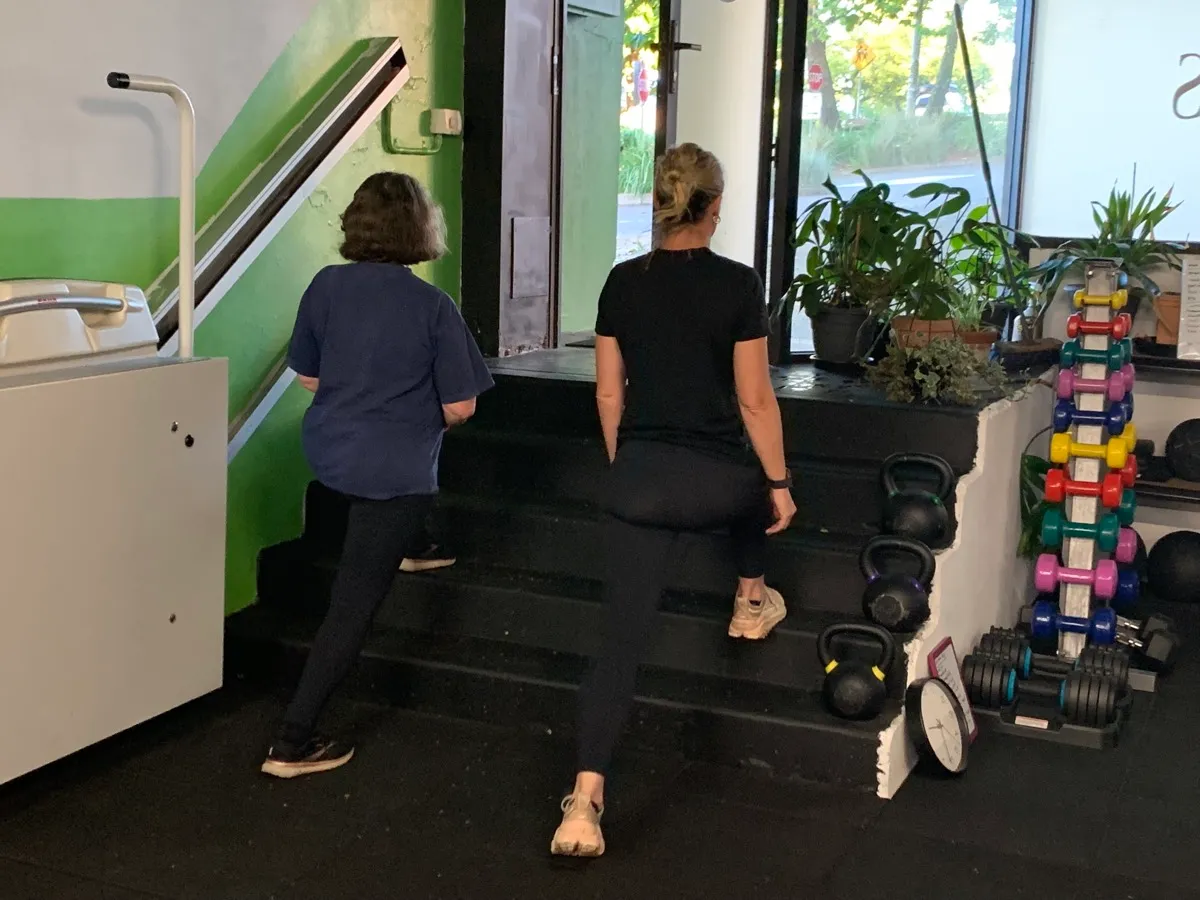 Two women walking up the steps into the studio, past the green wall.